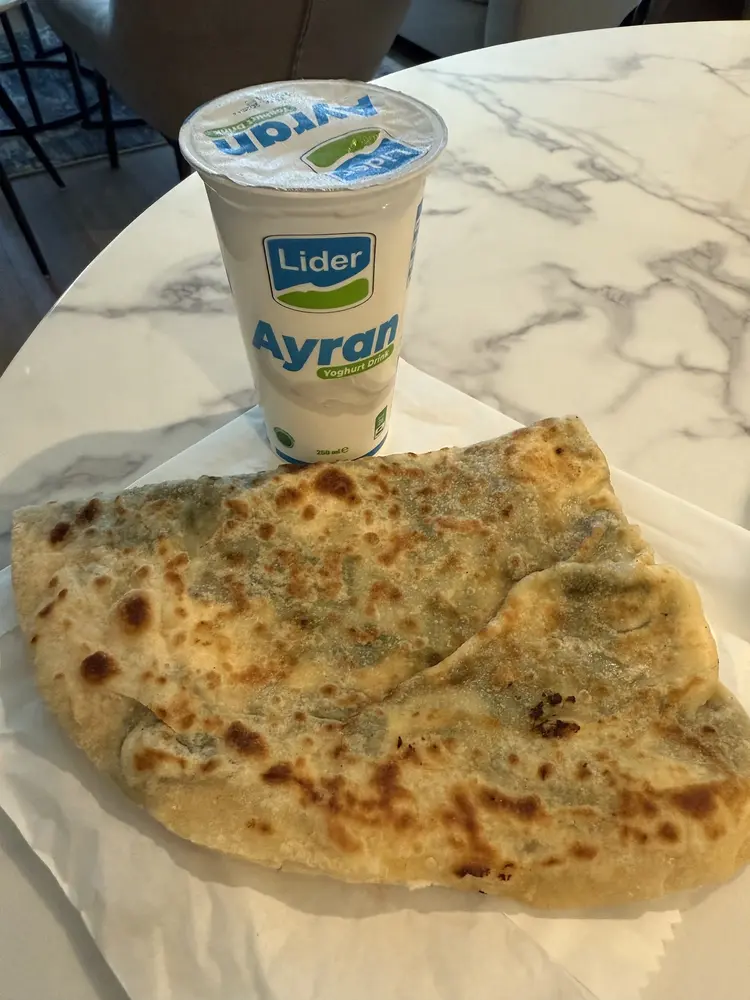 Folded gözleme flatbread on paper beside a chilled ayran yoghurt drink