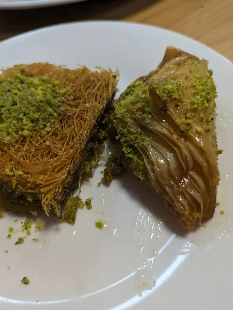 Two pieces of pistachio-topped baklava and shredded kadayıf on a white plate