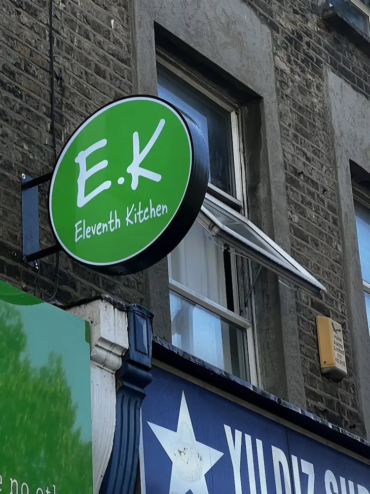 Round green Eleventh Kitchen sign projecting from a brick wall